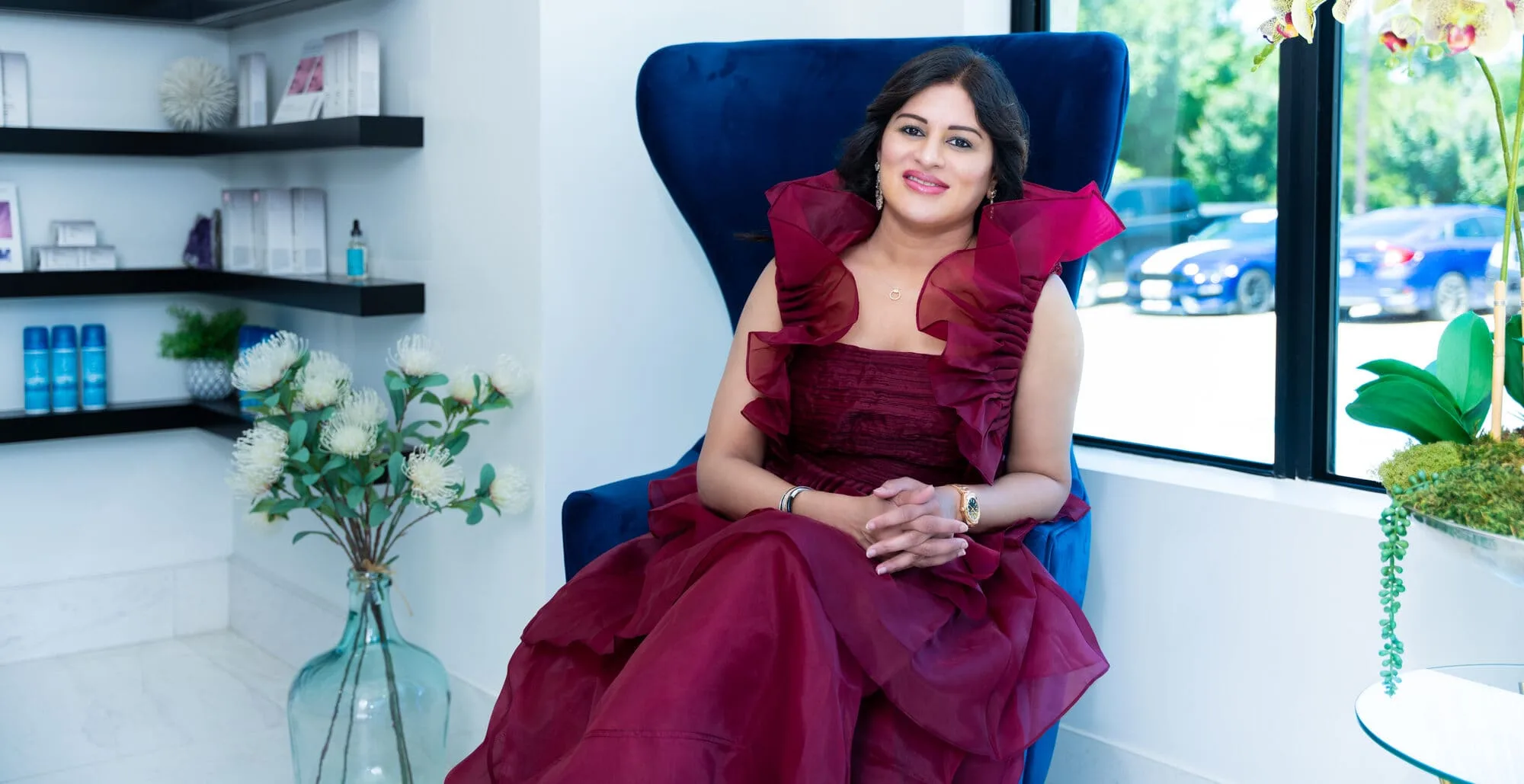 Dr. Haritha Mikkilineni, MD, seated in a blue velvet armchair beside the window in the retail area of the Medrein Health clinic in Southlake, TX