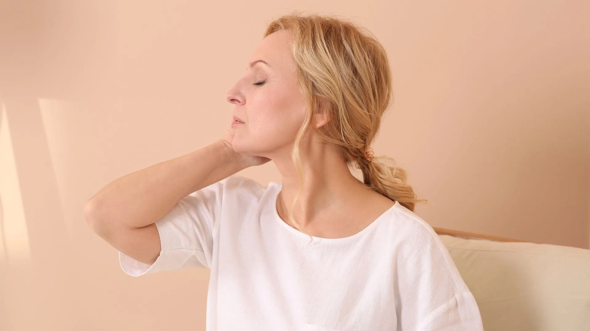 A woman in her fifties sitting with one hand at the back of her neck