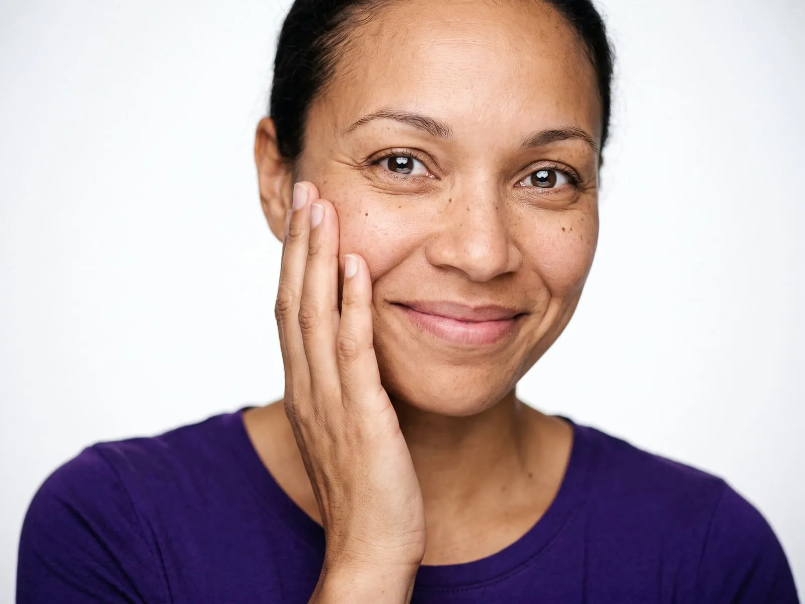 A woman in her forties with her hand resting against her cheek at close range, visible pores and uneven skin tone, the concern an aesthetic consultation at Medrein Health starts from
