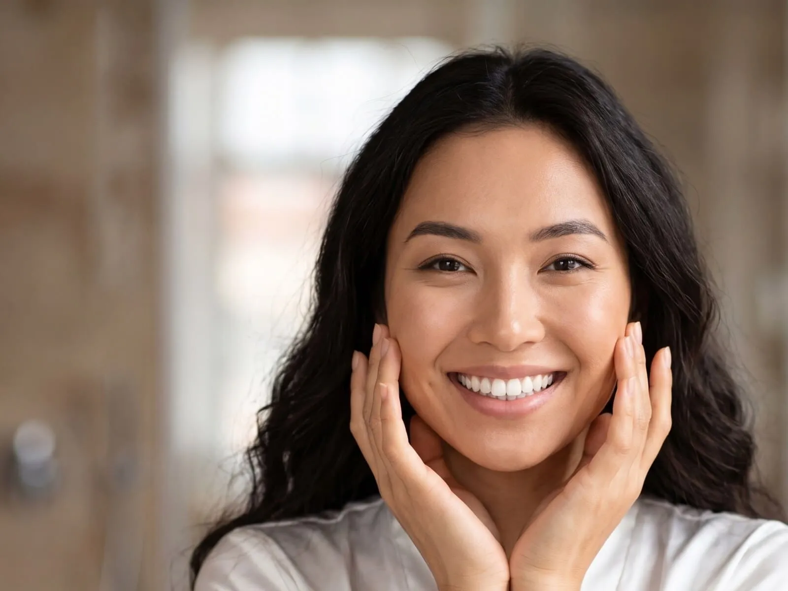 A woman in her late twenties with clear, healthy skin, her hands framing her face