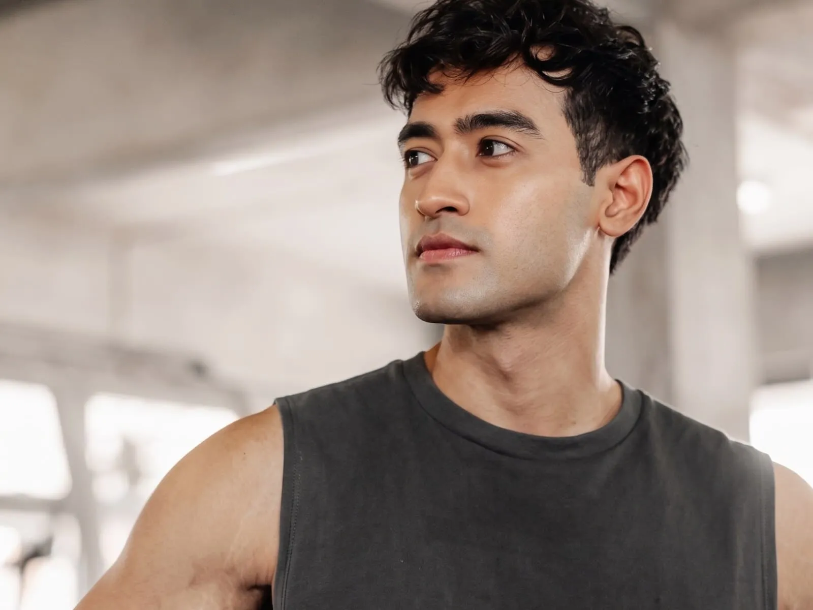 A man in his early thirties in a grey sleeveless top in a gym, his shoulder and upper arm in frame, the muscle GHRH peptides support