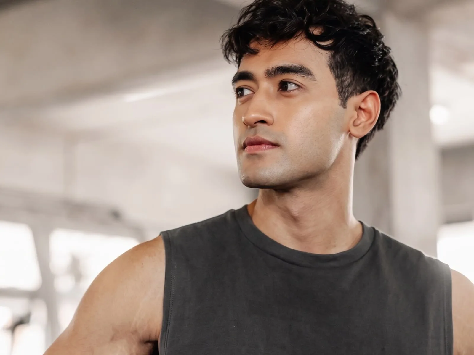 A man in his early thirties in a grey sleeveless top in a gym, shoulder and upper arm in frame, the muscle GHRH peptides act on